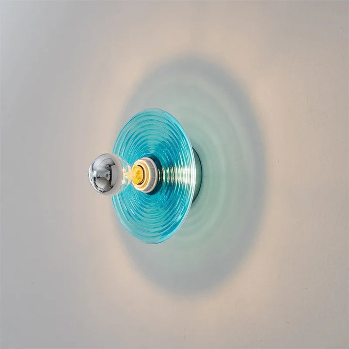 Wall-mounted light fixture with a blue glass shade on a neutral background
