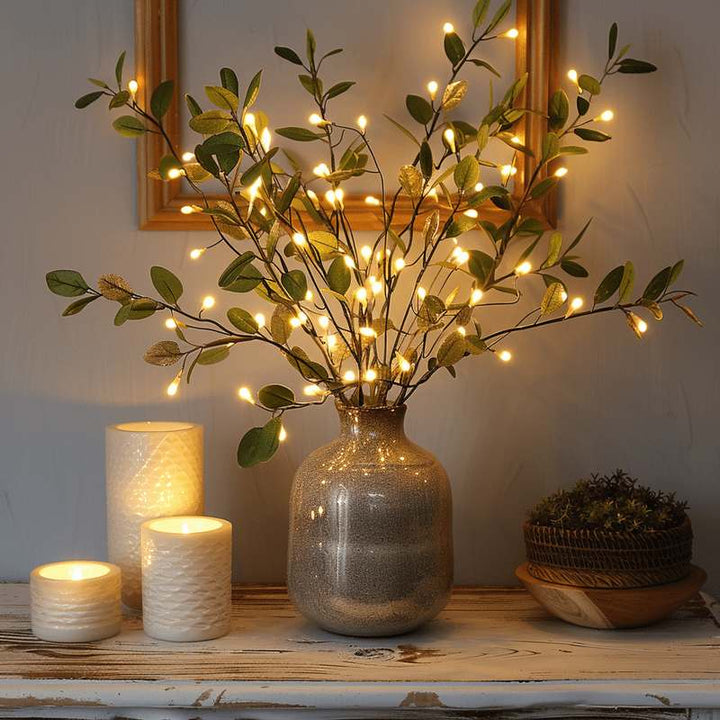 Illuminated Olive Branch decorative light in a glass vase, paired with white candles and rustic accents for elegant home styling.