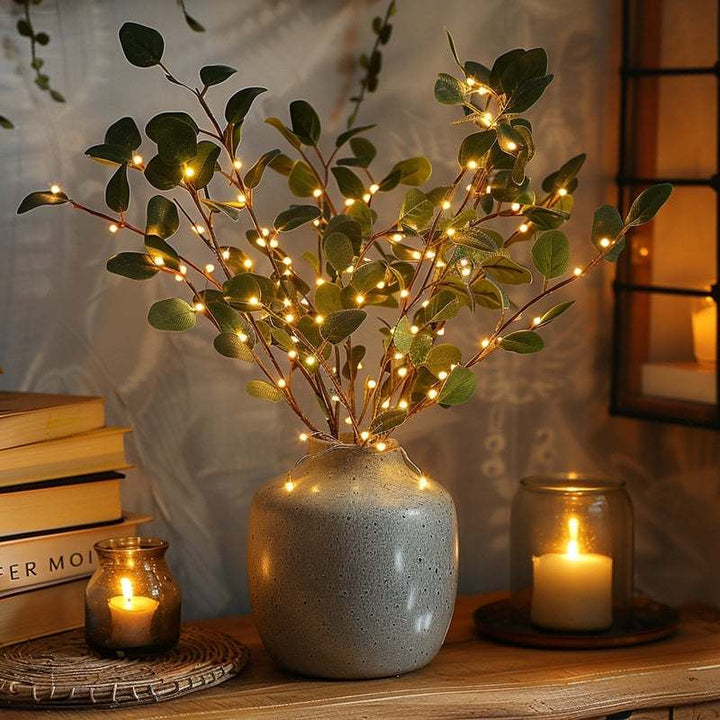 Glowing Olive Branch string light centerpiece in a stone vase, styled with candles and books for a warm and inviting setting.
