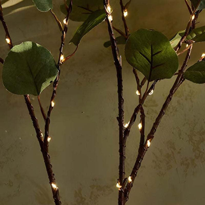 Close-up detail of Olive Branch fairy lights wrapped around stems, showcasing warm illumination against natural green leaves.