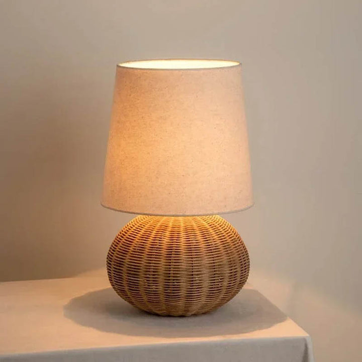 Small LUN rattan round table lamp lit up, soft ambient bedroom light with natural wicker base and linen shade
