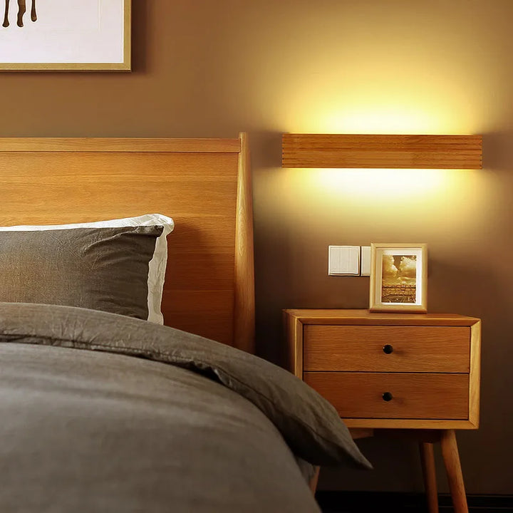 Wooden LYSE LED wall light mounted beside bed, creating cozy bedroom ambience