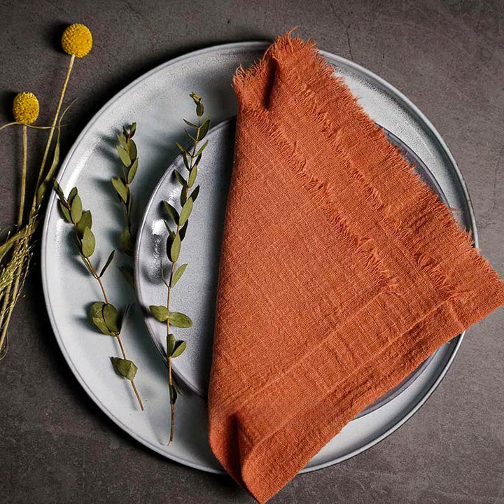 Clay ember cotton gauze napkin folded on ceramic plate with botanical accents, 41 × 41cm – soft and elegant for Scandinavian-style tables.