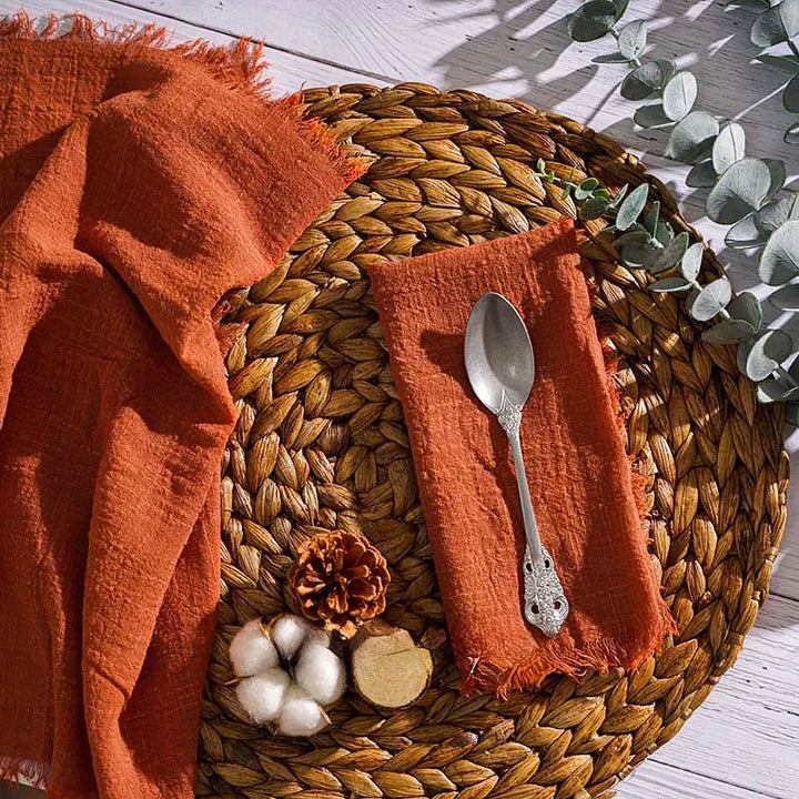 Clay Amber cotton gauze napkin with frayed edges on woven placemat, 16 x 16 inch – reusable dinner table accessory.