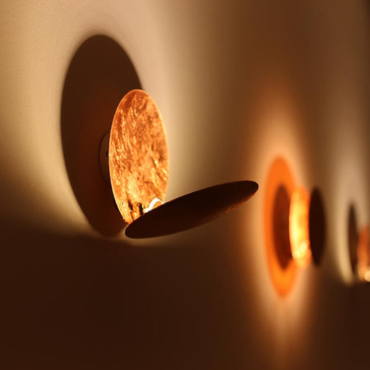 Side view of MÅNE Solar Eclipse Wall Light creating layered shadows and a golden ambient glow.