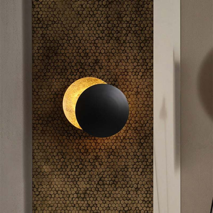 Black and gold MÅNE Solar Eclipse Wall Light resembling an eclipse, mounted on textured wall tiles.