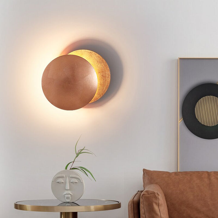 Copper MÅNE Solar Eclipse Wall Light with golden backplate, illuminating a modern living space.
