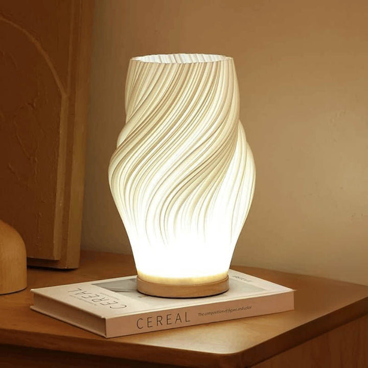 Curved MOLLEN 3D printed LED lamp on a coffee table book, softly lighting a minimalist interior corner.