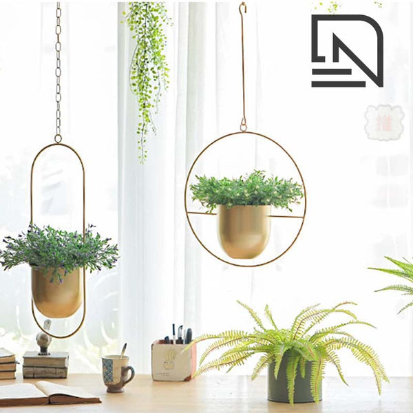 Hanging gold planters with green plants on a desk with a white curtain background