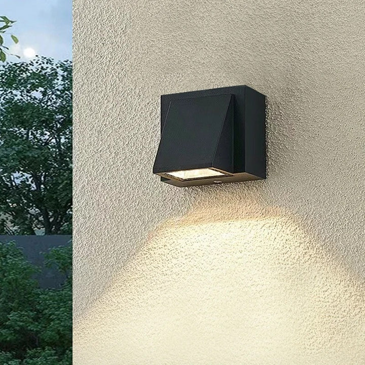 Black outdoor wall light fixture on a textured wall with greenery in the background