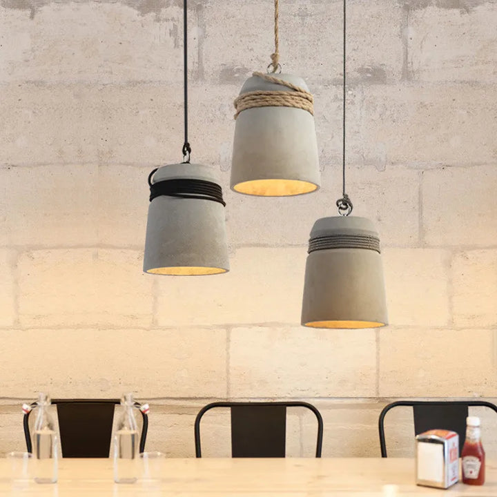 Three concrete pendant lights hanging above a dining table with a rustic wall background.