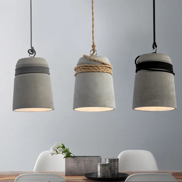 Three concrete pendant lights hanging above a dining table with a neutral background.