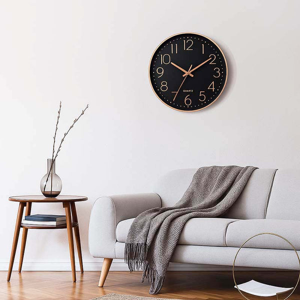 Wall clock on a white wall above a gray sofa with a wooden side table and vase.