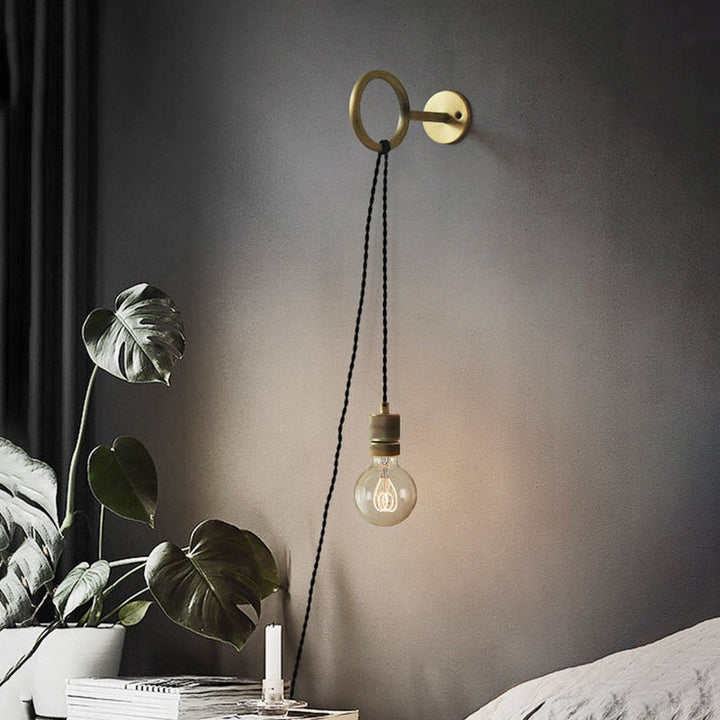 Modern wall-mounted light fixture with a hanging bulb on a dark wall.