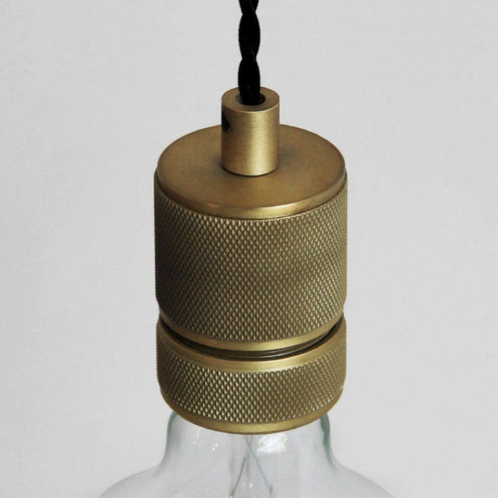 Brass textured lampshade on a clear glass base against a light gray background
