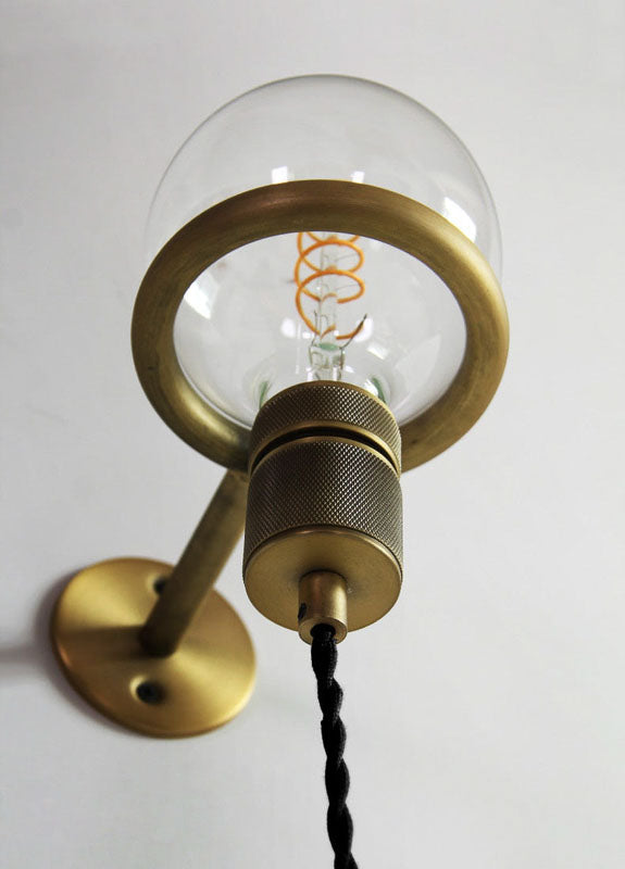 Brass wall-mounted light fixture with clear glass shade on a white background