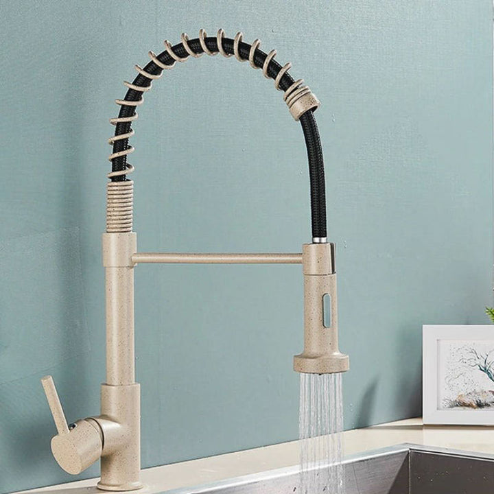 Beige kitchen tap with a pull-down spray head on a light blue wall background.