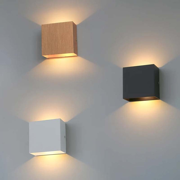 Three square wall lights in different colours on a grey wall.