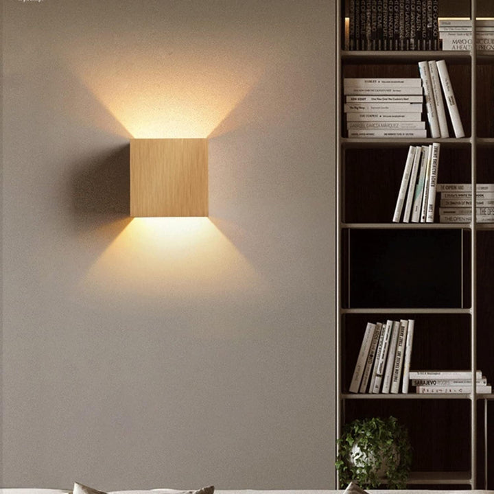Modern wall sconce lighting fixture on a neutral wall with a bookshelf in the background.