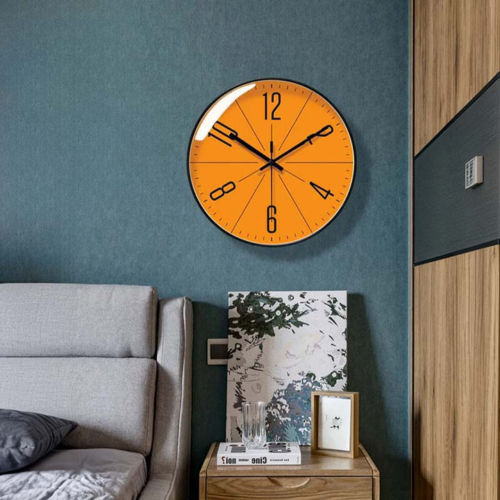 Orange wall clock on a blue wall above a bed in a bedroom setting.