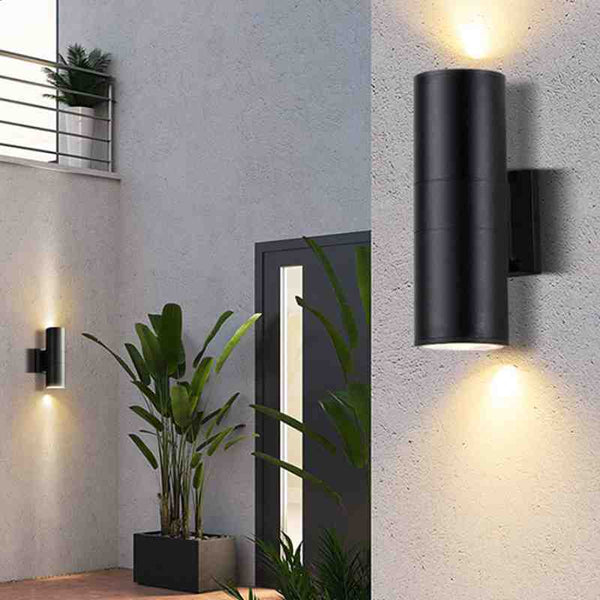 Black up and down LED wall light installed on modern patio wall beside green plants.