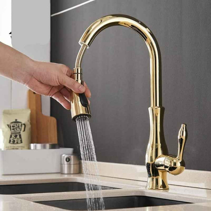Gold Pull-Out kitchen faucet with water flowing into a sink, set against a kitchen background.