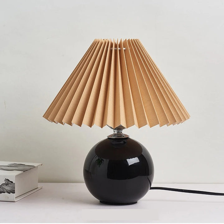 Black ceramic lamp with tan pleated shade, modern bedside light for moody and minimal decor schemes.