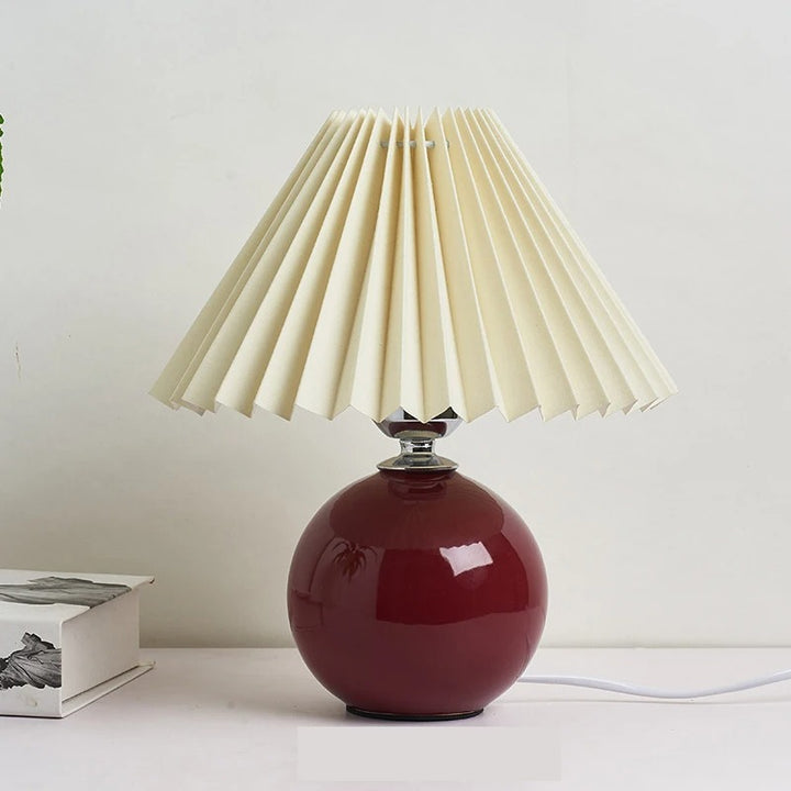 Red bedside lamp with round ceramic base and pleated shade, stylish lighting for bedroom or lounge.