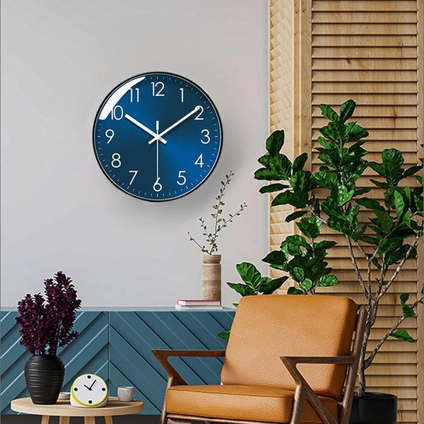 Blue modern wall clock on a wall with a chair, plants, and small table in the foreground.