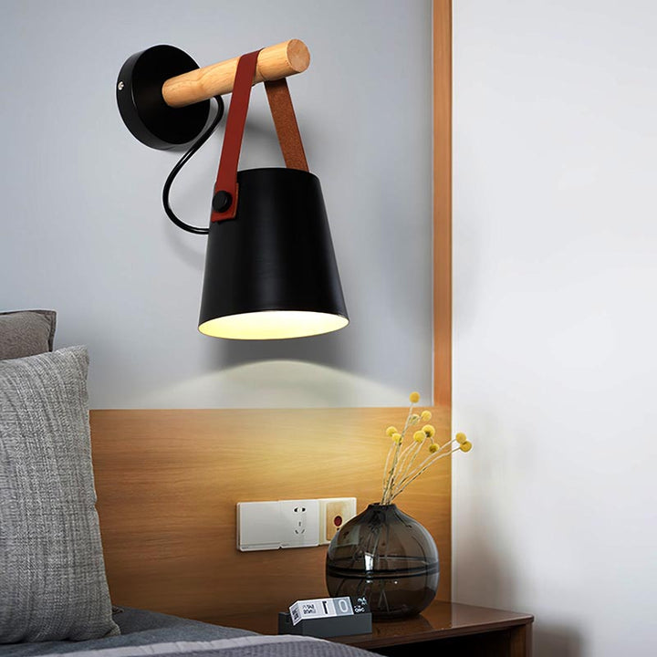Modern wall lamp with black shade and wooden arm in a bedroom setting.