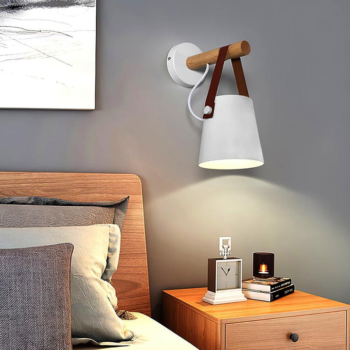 Modern wall lamp with wooden accent on a bedroom wall, next to a bed and nightstand.