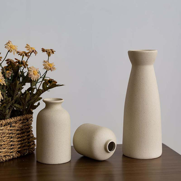 Three beige ceramic vases and a basket with dried flowers on a wooden surface.