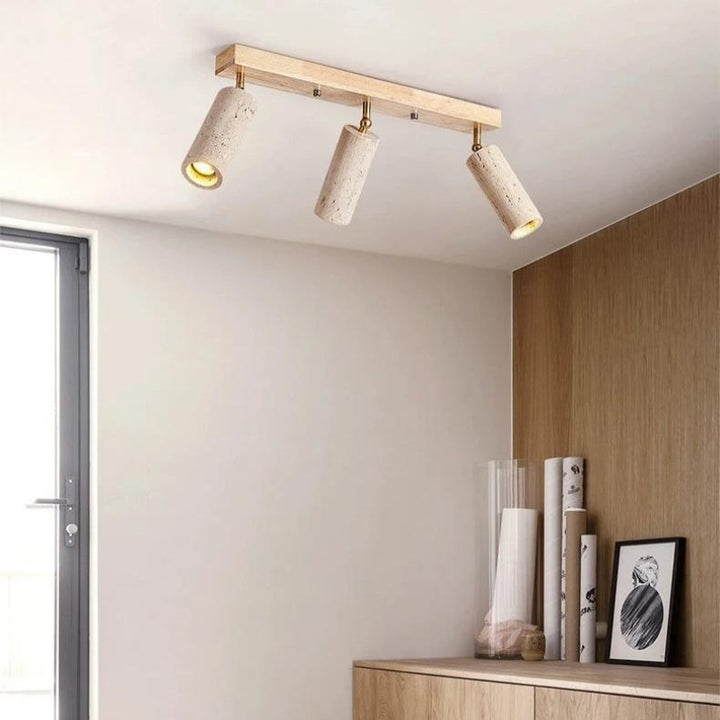 Ceiling light fixture with three cylindrical lights in a room with a wooden shelf and window.