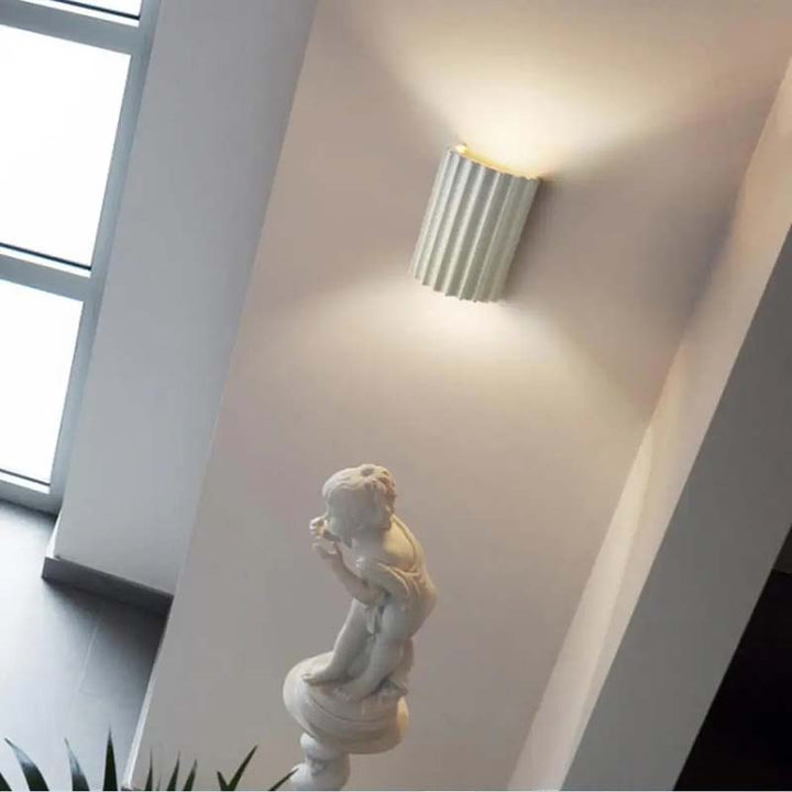 Modern white Wall-mounted light fixture on a white wall with a statue in the foreground