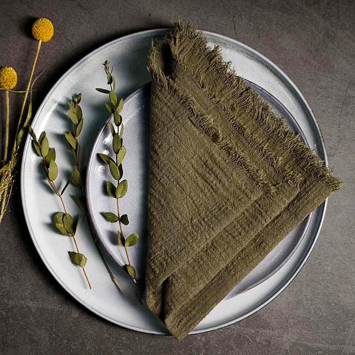 Olive green cotton gauze napkin folded on ceramic plate with botanical accents, 41 × 41cm – soft and elegant for Scandinavian-style tables.