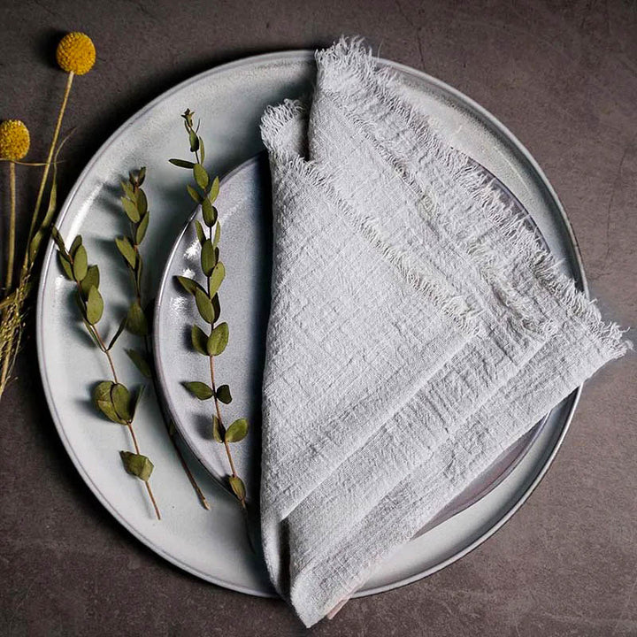 Dust blue cotton gauze napkin folded on ceramic plate with botanical accents, 41 × 41cm – soft and elegant for Scandinavian-style tables.