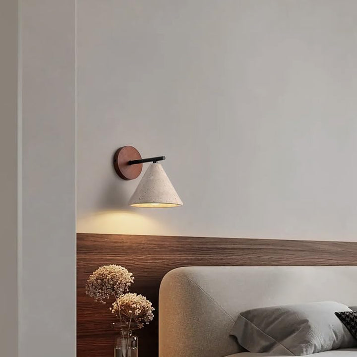 Modern wall sconce on a neutral wall above a bed with wooden headboard