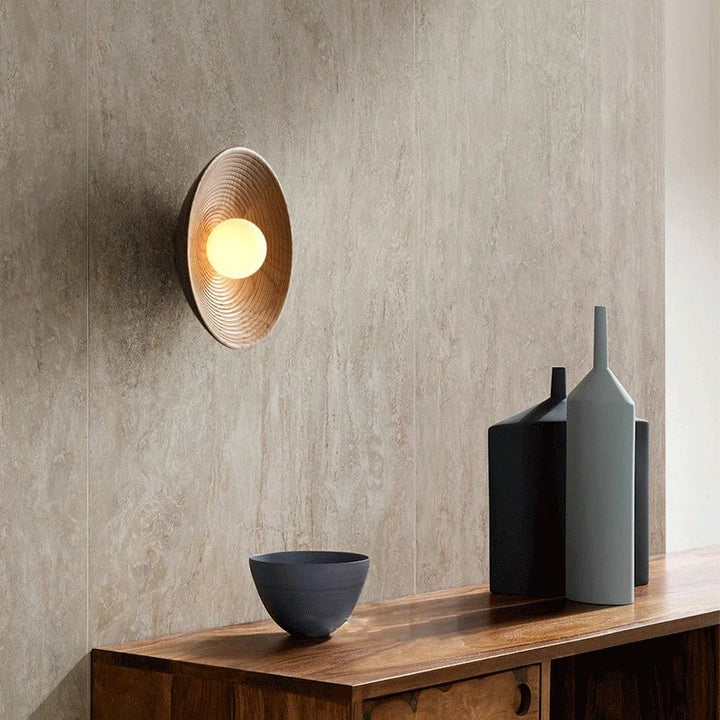  Natural wood wall lamp mounted above a wooden sideboard with minimalist decor in a Nordic-inspired living space.