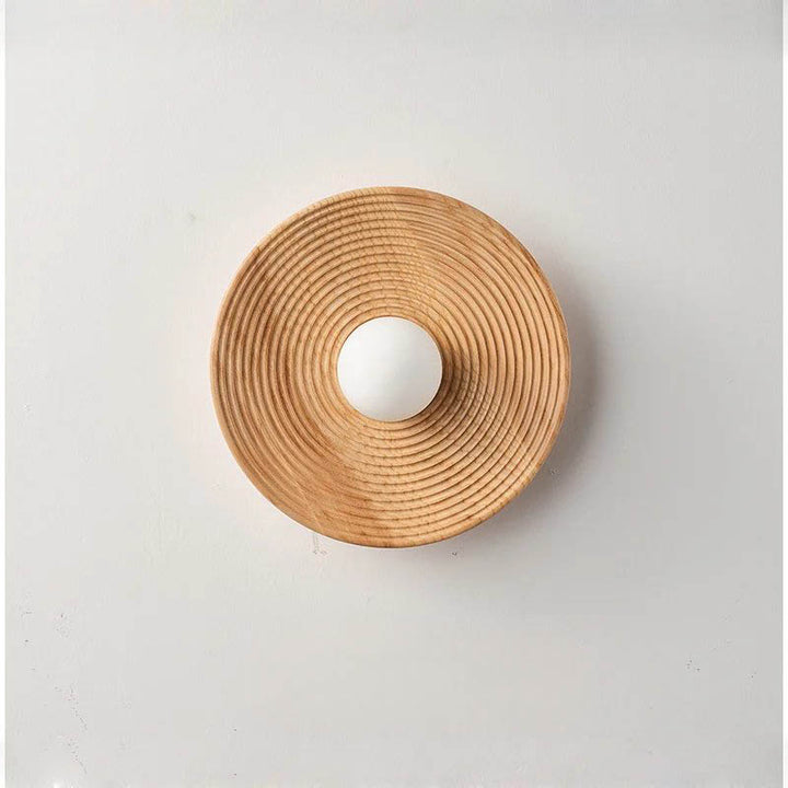 Natural wood wall lamp against a white wall with the light turned off, highlighting the carved wooden texture and form.