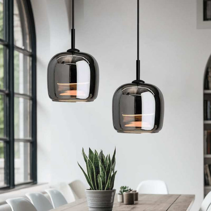 Two modern nordic glass pendant lights hanging above a dining table with a plant in the foreground.