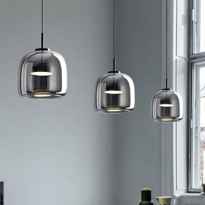 Three modern dimmable pendant lights with smoked glass shades hanging in a room with a window.