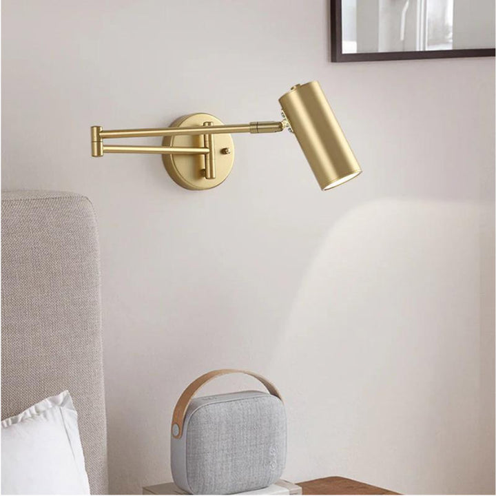 Foldable Gold wall-mounted lamp on a white wall with a gray speaker below.