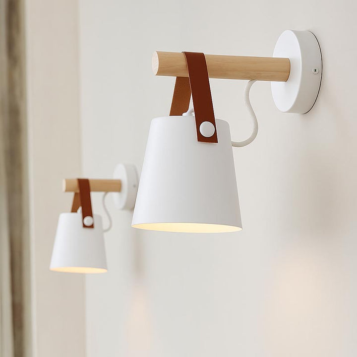 Wall-mounted lamp with white shade and brown leather strap on a light background