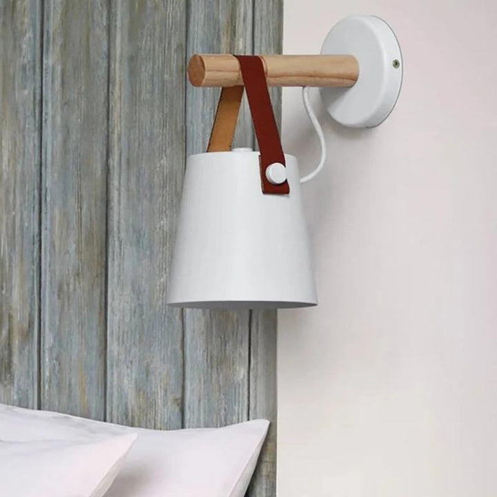 Wall-mounted lamp with white shade, wooden arm, and leather strap against a wooden panel background.