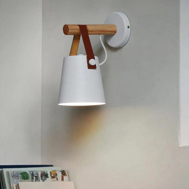 Wall-mounted lamp with white shade, wooden handle, and red strap on a light gray wall.