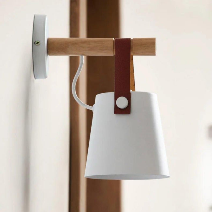 Wall-mounted lamp with white shade, wooden arm, and leather strap on a neutral background