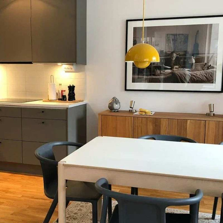 Modern kitchen with a dining table and chairs, featuring a yellow pendant light and framed picture on the wall.