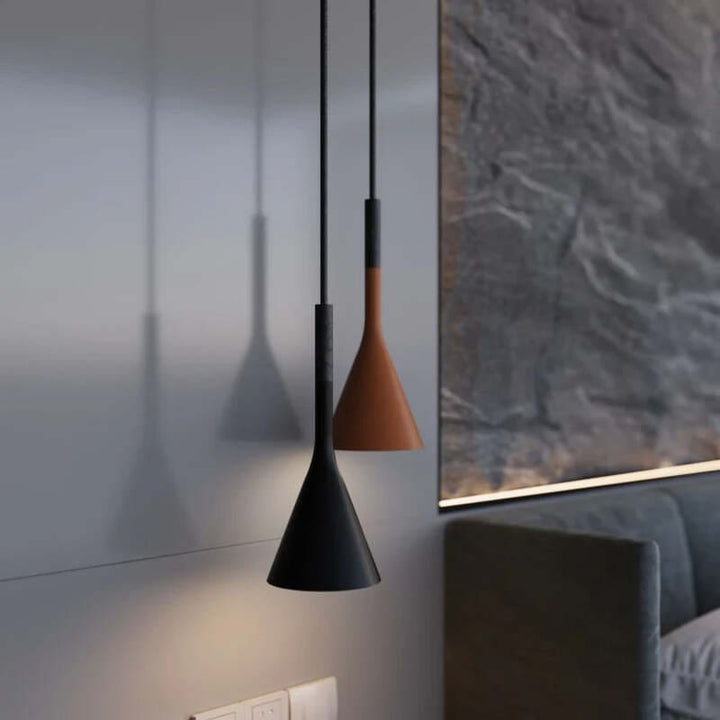 Two pendant lights, one black and one brown, hanging in a room with a window and sofa.