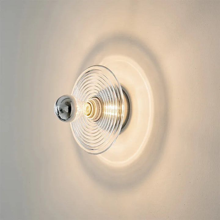 Wall-mounted light fixture with clear glass shade on a neutral background
