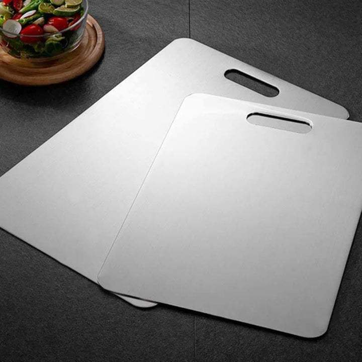 Two white stainless steel cutting boards on a dark surface with a bowl of salad in the corner.